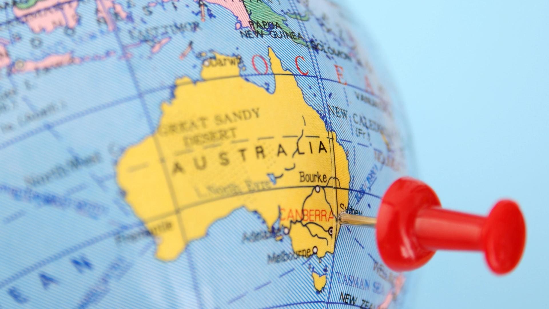 Close-up of a globe with a red pushpin marking Canberra, Australia, emphasizing location and geography
