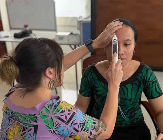 medical student using handheld device to check another's forehead in a clinical setting.